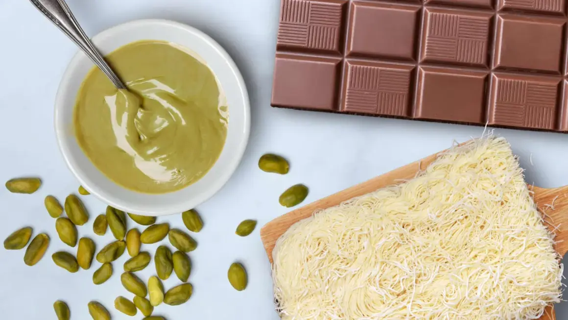 Zutaten für ein **Rezept Dubai Schokolade**: Pistaziencreme, Schokoriegel, Kataifi-Teig und ganze Pistazien.