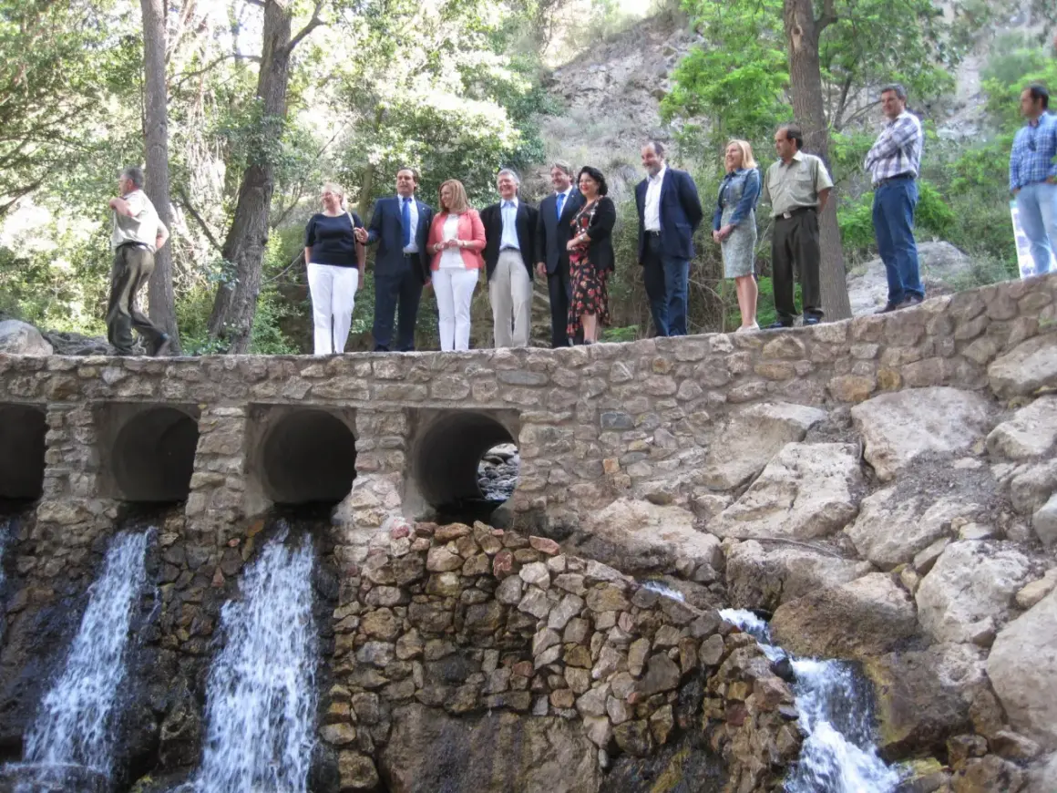 Un grupo de personas celebra en el lugar donde nace el río Andarax, con cascadas cayendo bajo un puente de piedra.