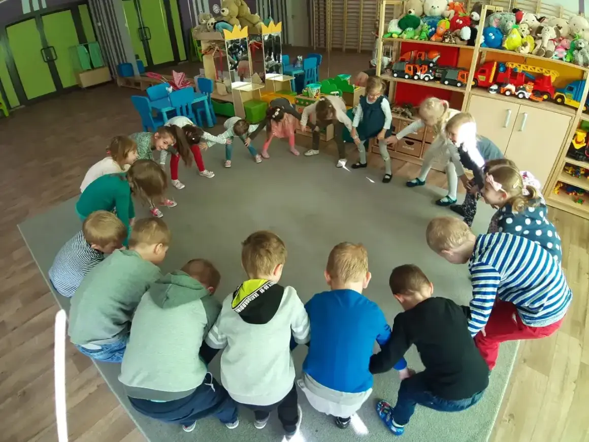 Dzieci w przedszkolu biorą udział w zabawach integracyjnych, tworząc krąg i wykonując ćwiczenia.