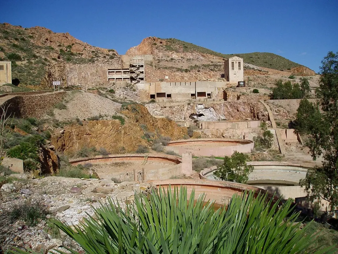 Ruinas de las minas Rodalquilar, con edificios abandonados y balsas circulares en un paisaje árido bajo un cielo azul.