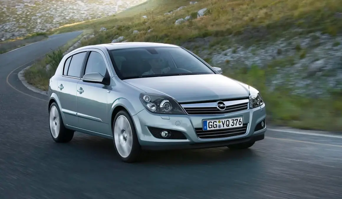 Srebrny Opel Astra GTC z kierowcą za kierownicą pokonuje zakręt na górskiej drodze.