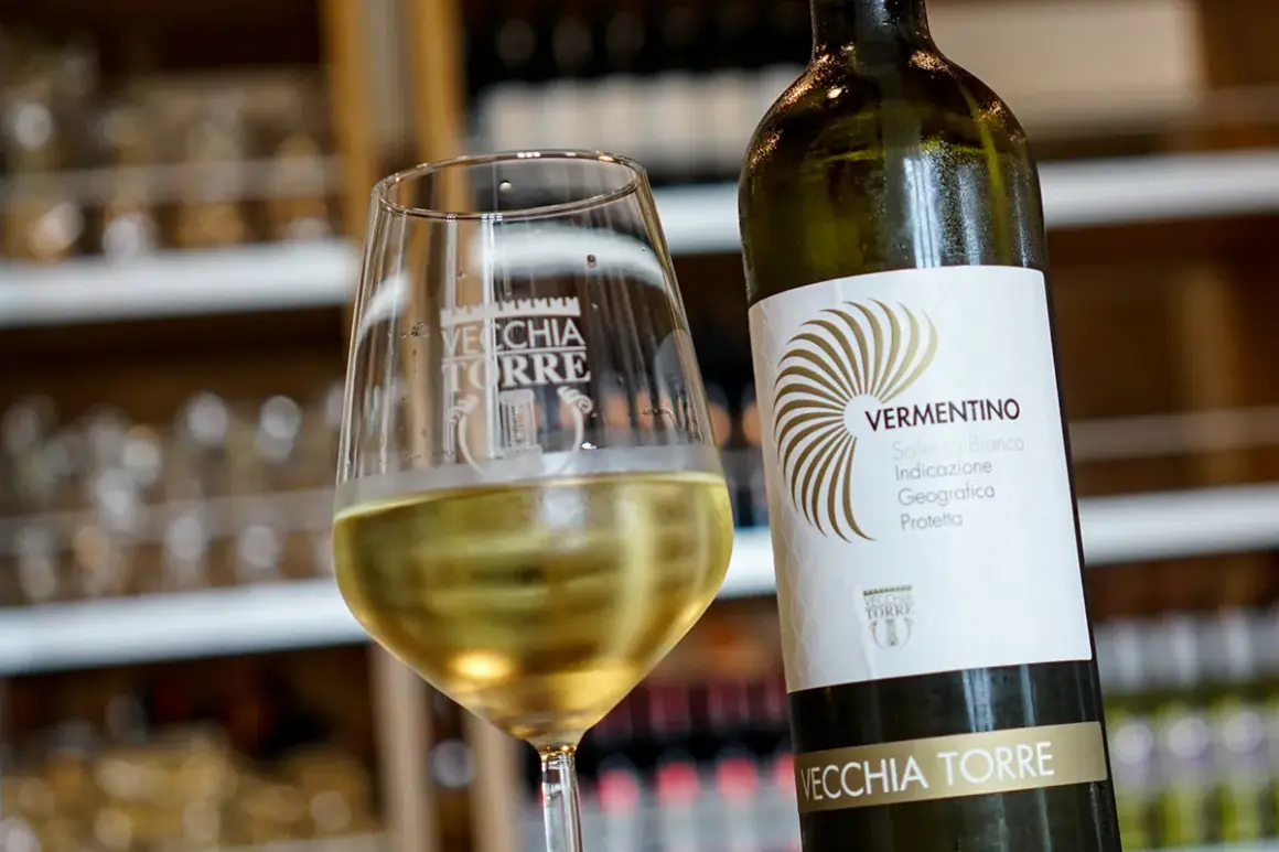 Un bicchiere di vino bianco, il vermentino è frizzante, accanto alla bottiglia Vecchia Torre.