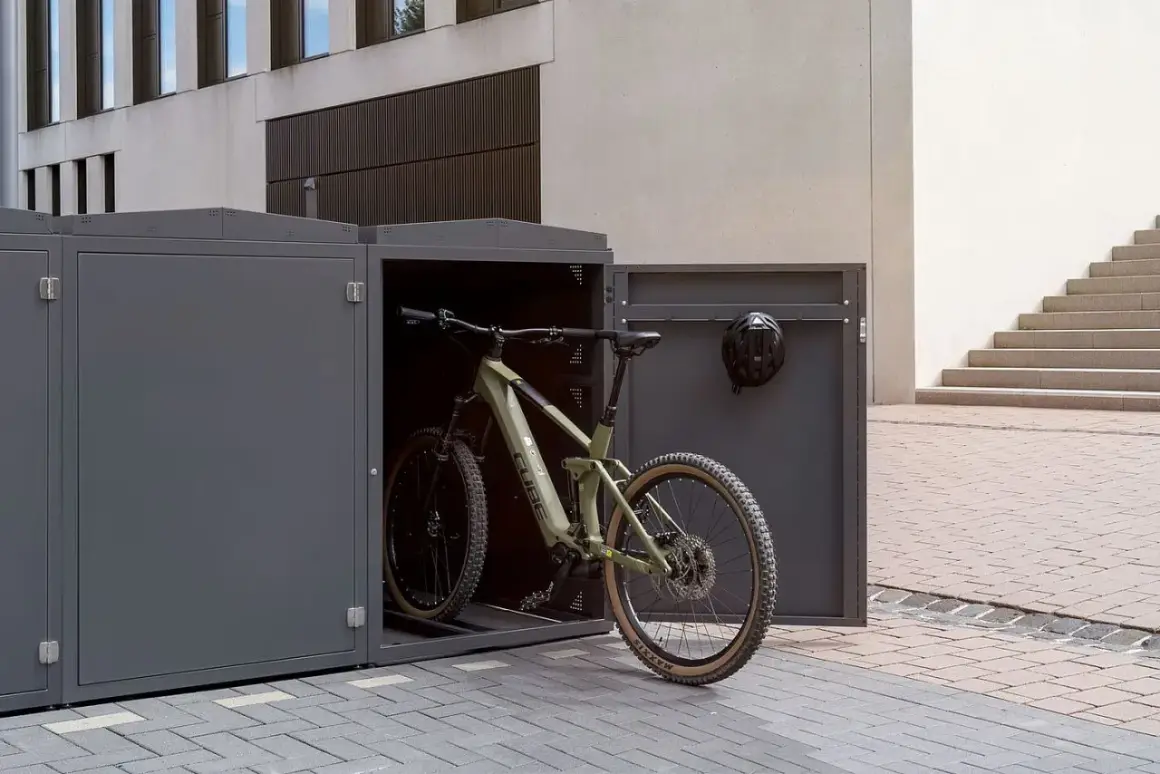 Ein grünes Mountainbike steht in einem modernen, grauen Fahrrad-Stellplatz. Ein Helm hängt an der Tür.
