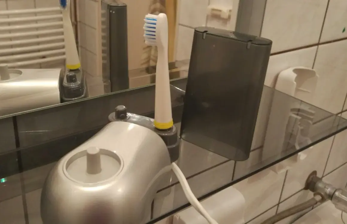 Elektroniczna szczoteczka do zębów i jej wymienna końcówka stoją na szklanej półce, pokazując, jak przechowywać szczoteczki do zębów w łazience.