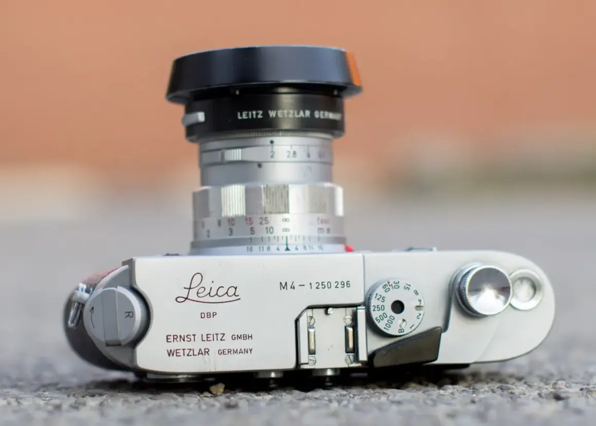 A Leica M4 camera with a Leitz Wetzlar lens. The camera body shows "Leica M4" and "Ernst Leitz GmbH Wetzlar Germany." The lens has aperture markings and a focus ring. The framelines are not visible in this shot.