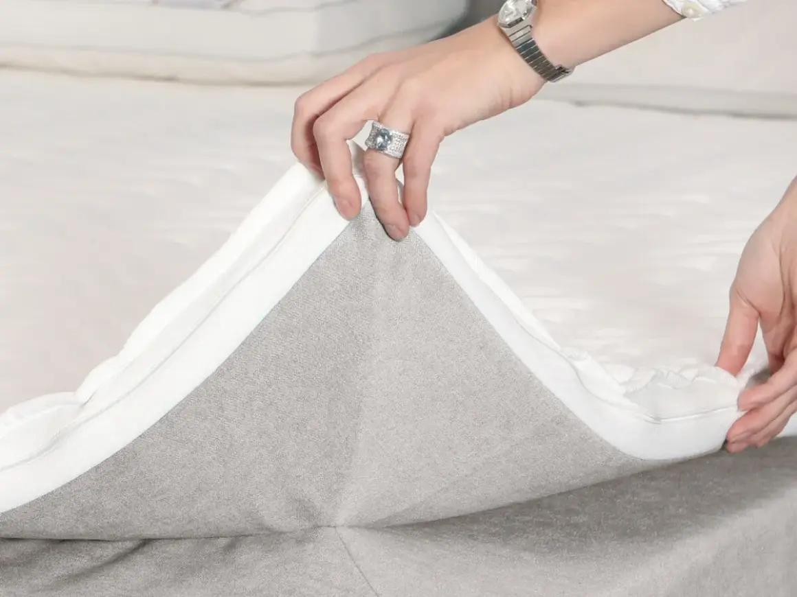 Hände ziehen den Reißverschluss eines Toppers ab, um die **Boxspringbett Pflege** zu erleichtern.