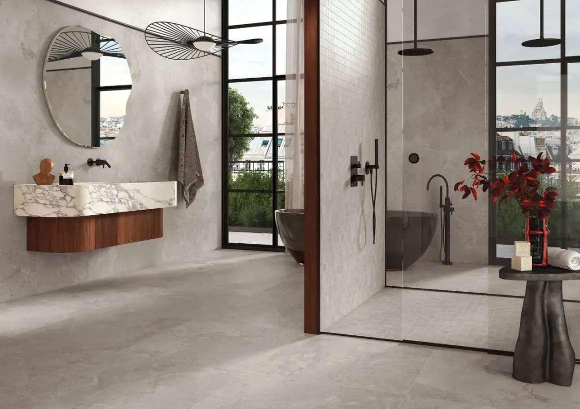 Salle de bain moderne avec baignoire îlot, douche vitrée et lavabo suspendu. La faïence grise habille les murs et le sol, créant une ambiance épurée et luxueuse.