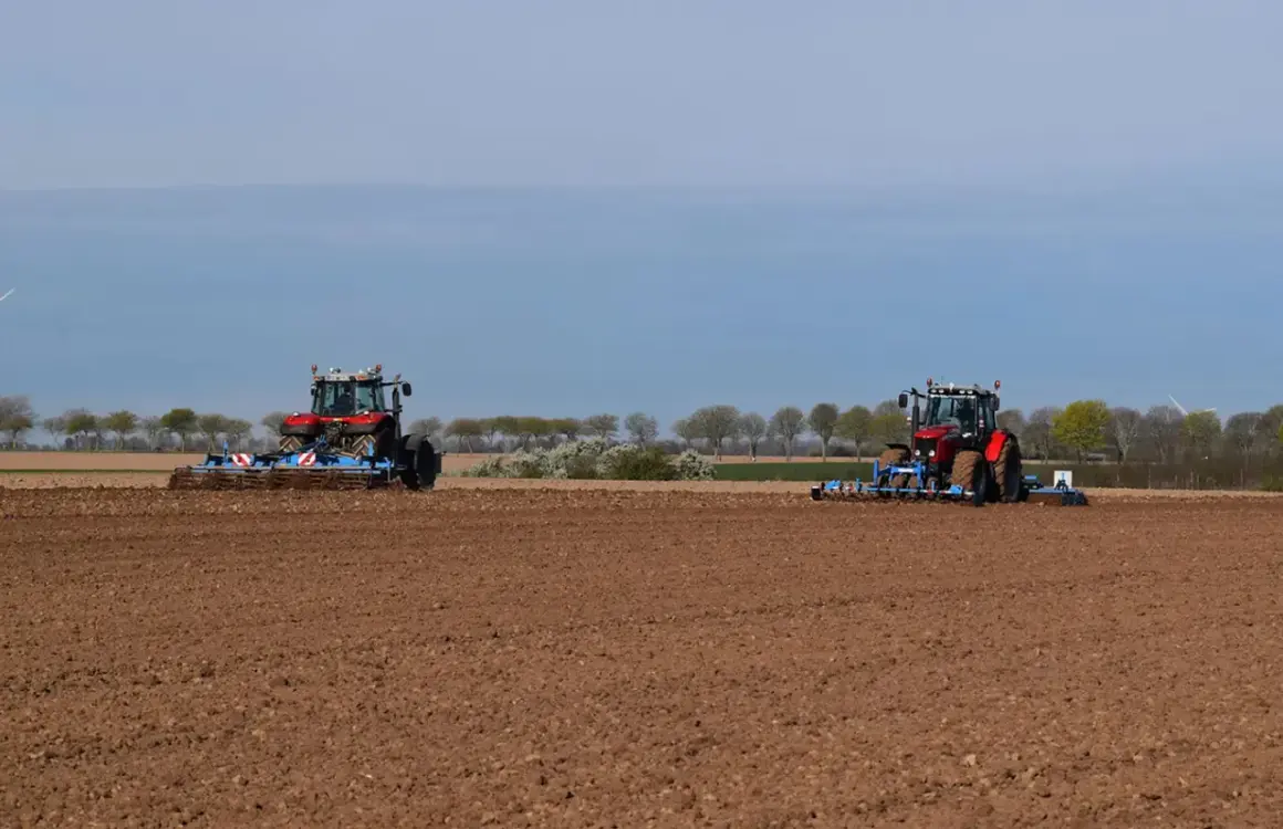 Deux tracteurs préparent le sol pour la culture du lin. Le champ est labouré, prêt pour les semis.