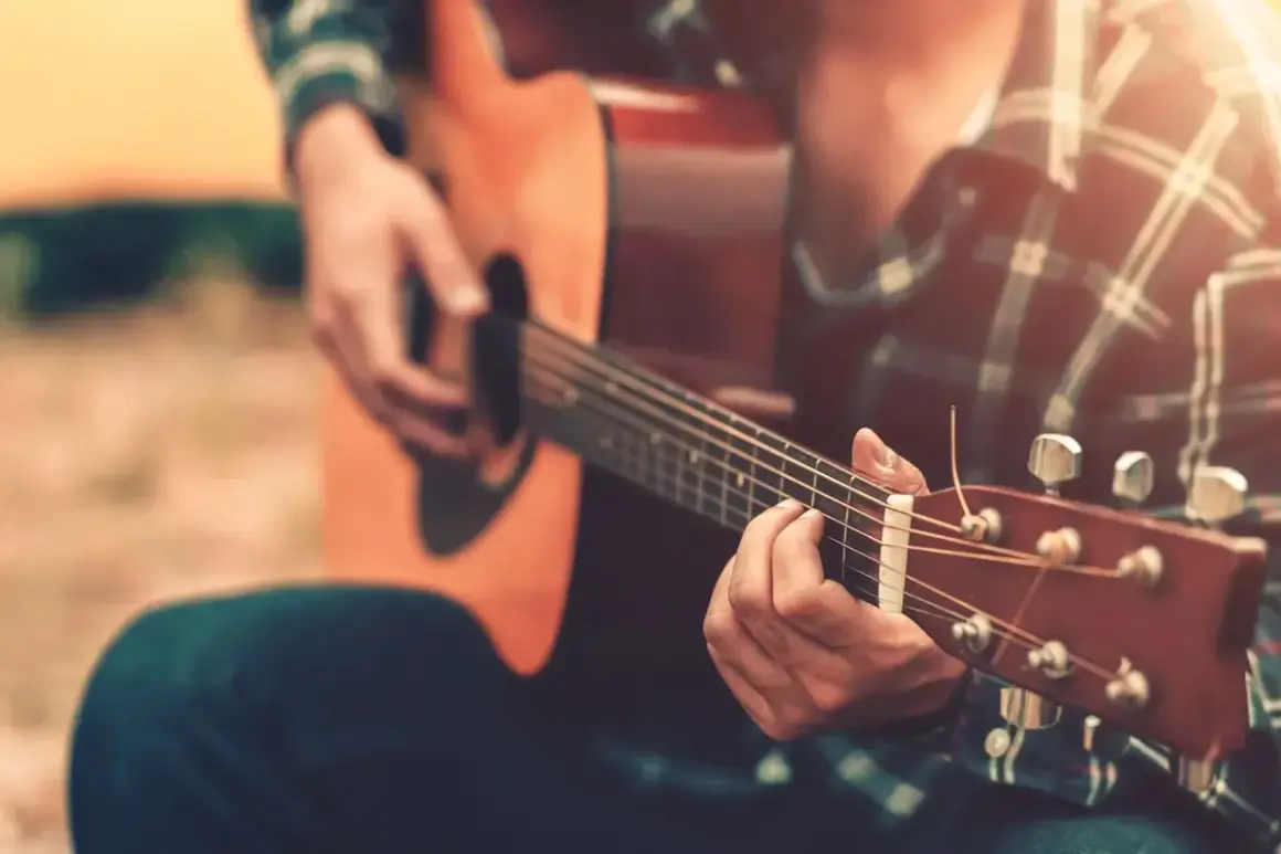 Un uomo con una camicia a quadri suona la chitarra acustica, creando una canzone per salutare colleghi.