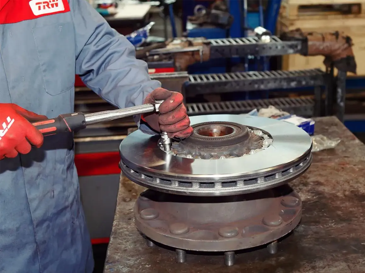 Mechanik w czerwonych rękawicach dokręca śruby podczas wymiany tarcz hamulcowych.