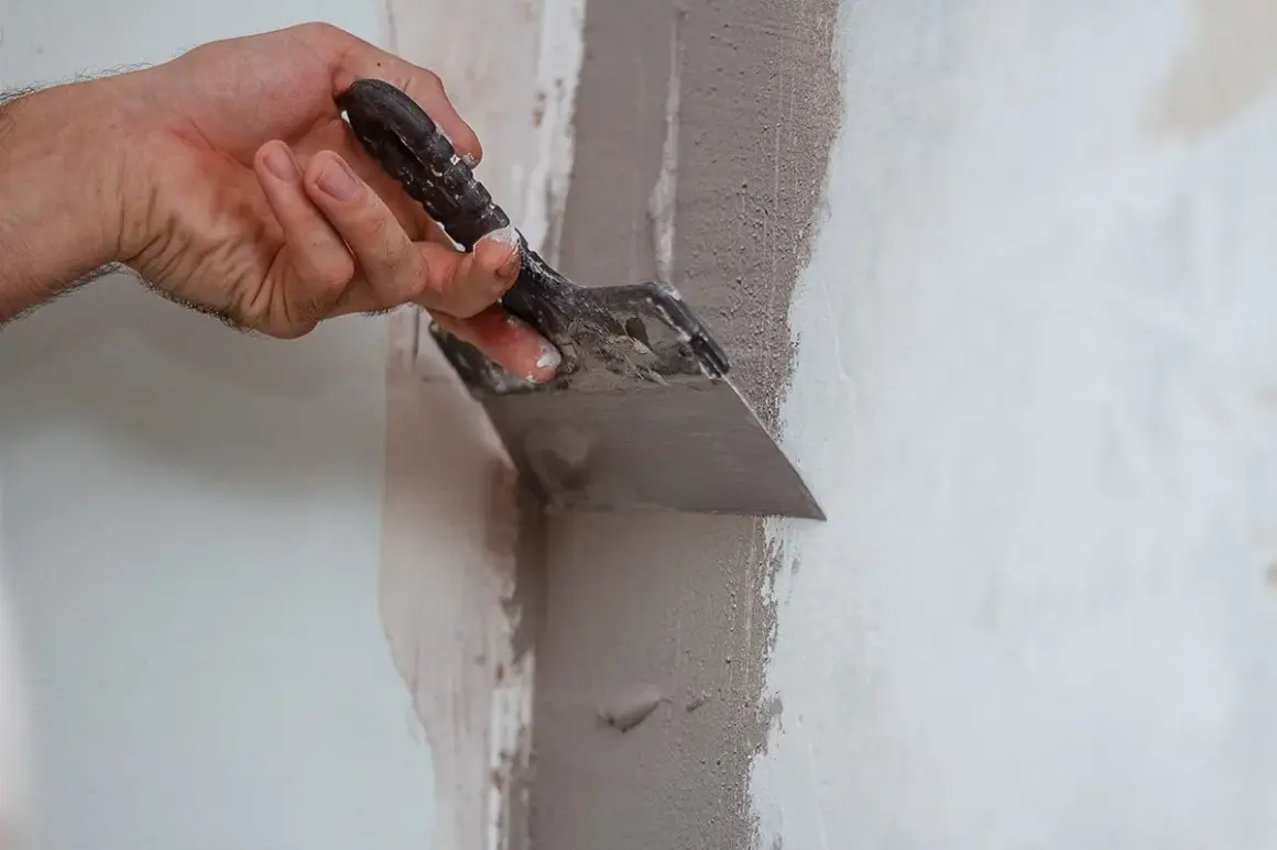 Mano con spatola riempie un buco nel muro con stucco, riparando la parete.