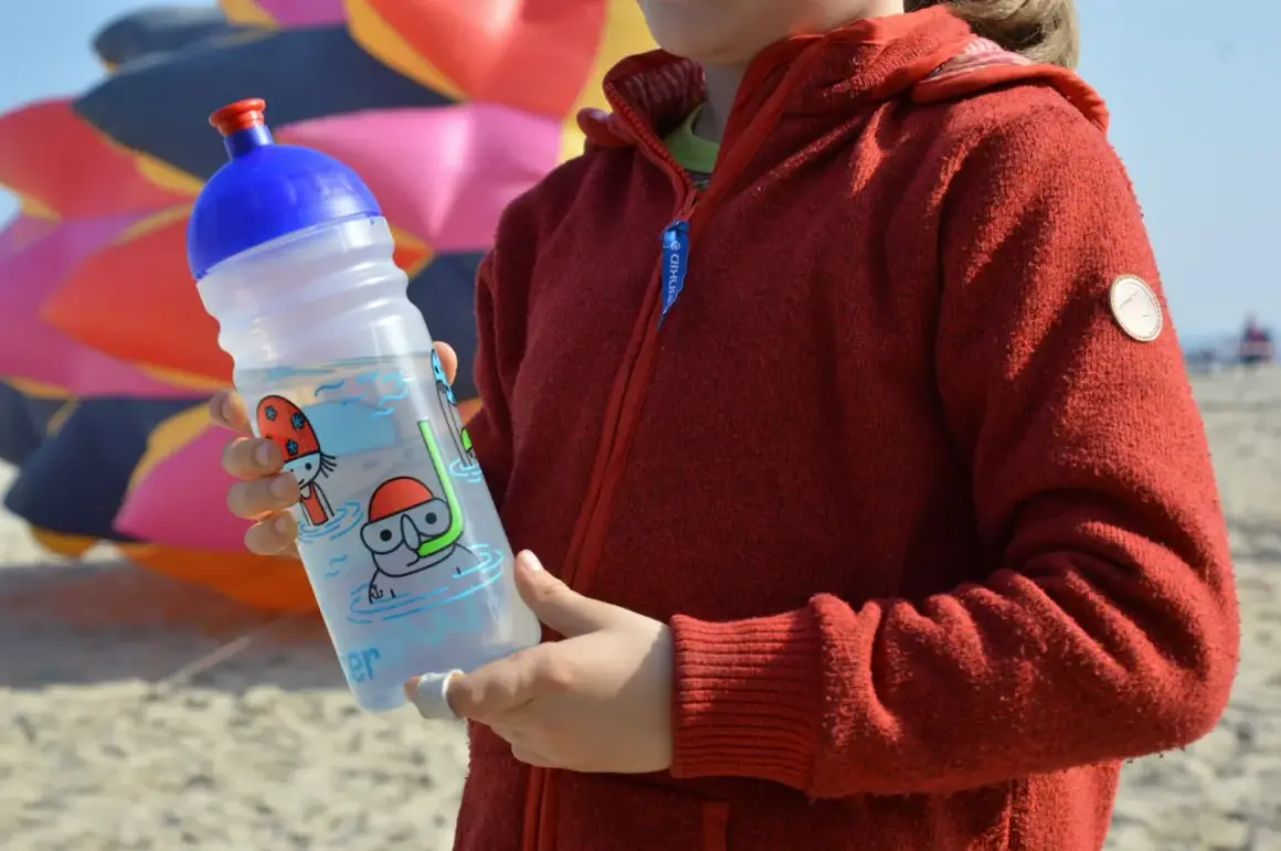 Kind hält eine isybe trinkflasche mit Tauchermotiv. Im Hintergrund bunter Drachen.