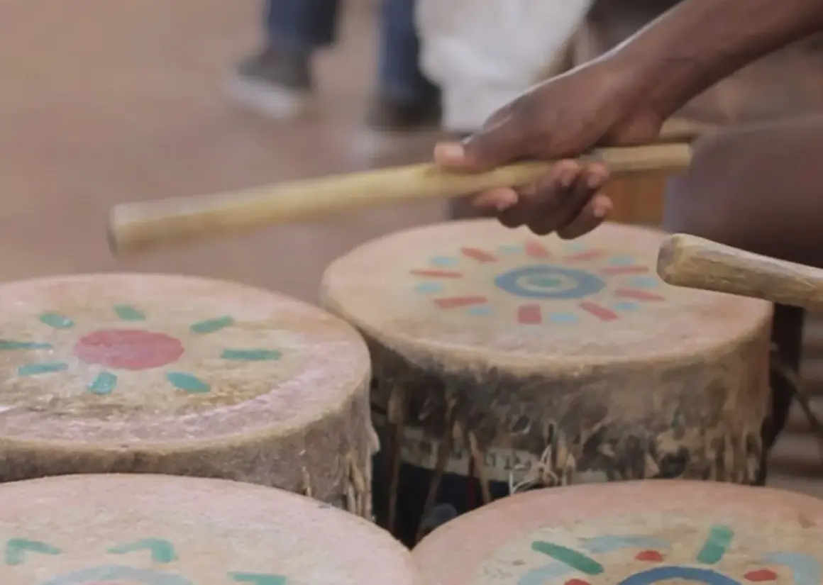Mani che percuotono tamburi decorati con motivi solari, creando la vibrante musica africana.