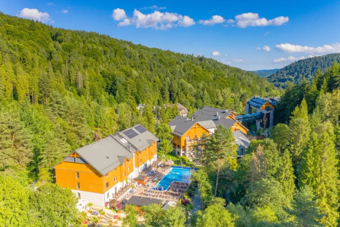 Idealne atrakcje na majówkę: kompleks hotelowy w otoczeniu zielonych lasów, z basenem i miejscami do wypoczynku.