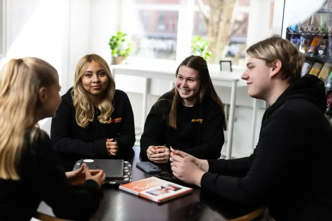 Fyra elever från Praktiska gymnasiet Kristianstad sitter samlade runt ett bord och samtalar.