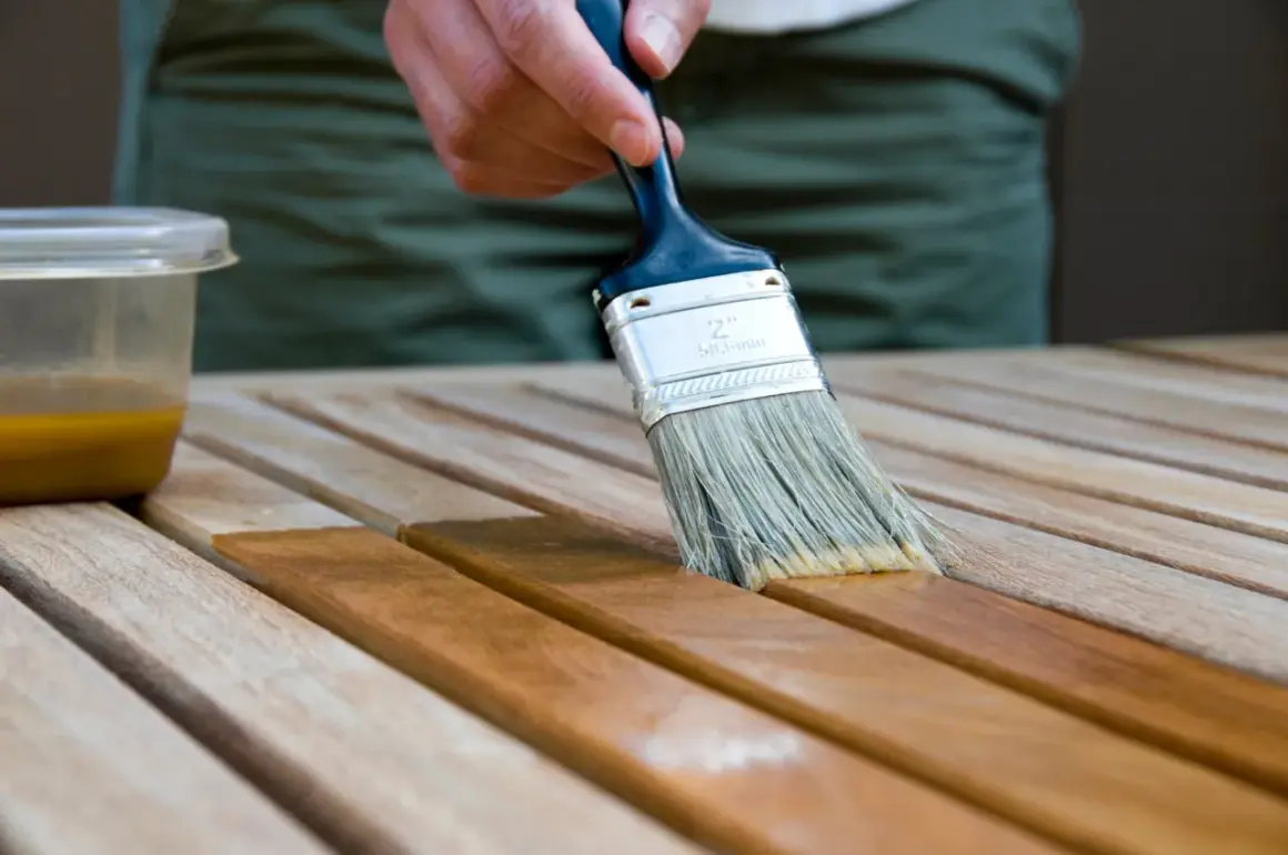 Application d'une lasure acrylique ou glycéro sur des lattes de bois. La brosse dépose le produit, transformant le bois clair en une teinte plus foncée et riche.