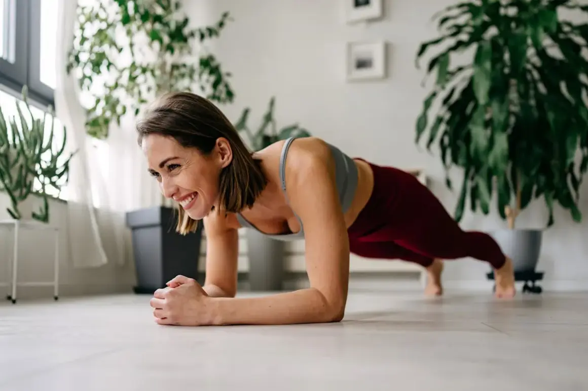 Femme souriante en position de planche, un excellent exercice ventre pour renforcer son corps à la maison.