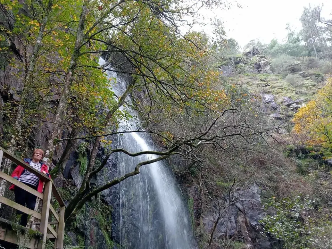 Mujer observa una impresionante cascada de agua caída en un entorno boscoso otoñal.