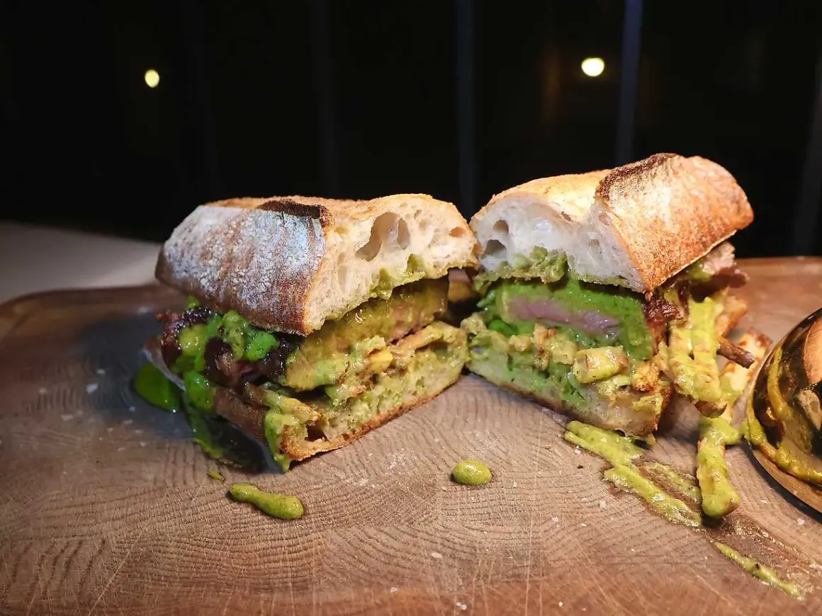 En saftig steak sandwich med avokado och en grön sås, upplagd på en träskärbräda.