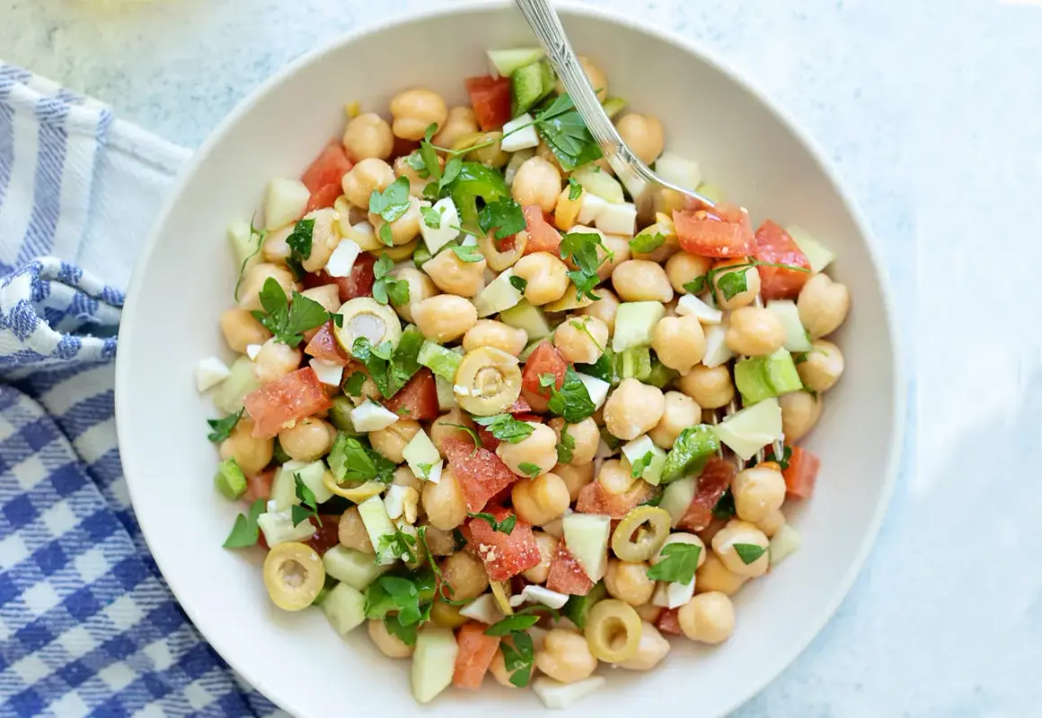 Ensalada de garbanzos fresca con tomate, pepino, aceitunas y perejil, lista para disfrutar.