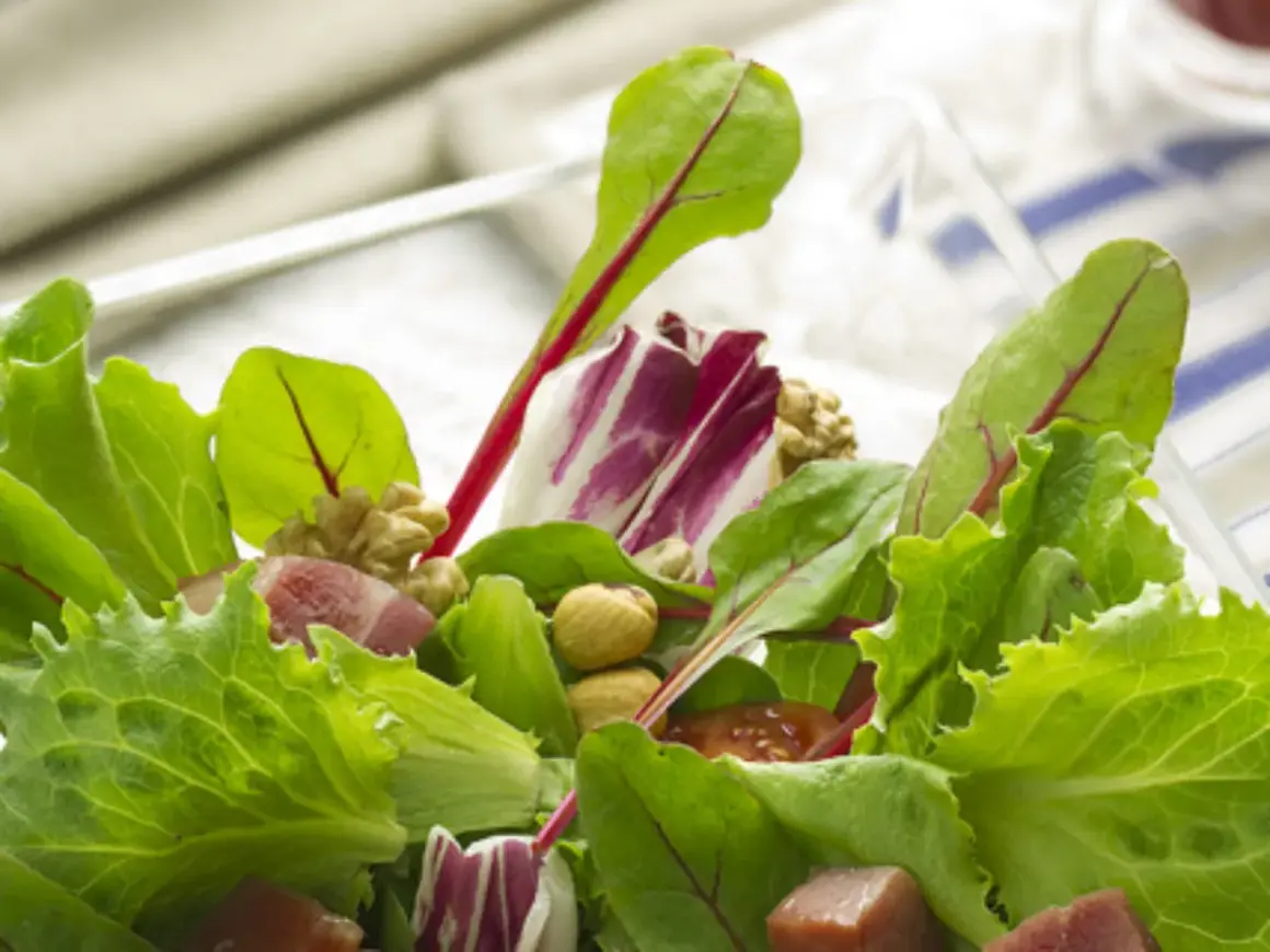 Ensalada fresca con brotes tiernos, nueces y trozos de jamón.