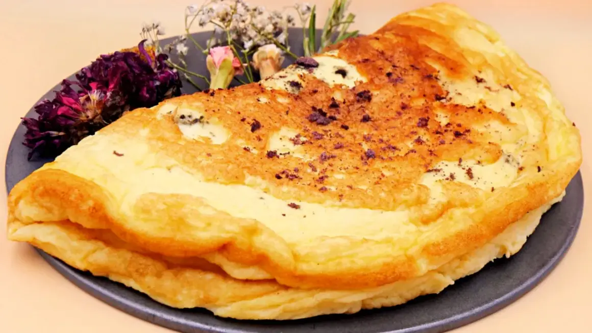 Puszysty omlet dla niemowlaka, delikatnie przyrumieniony, z ozdobnymi suszonymi kwiatami na talerzu.