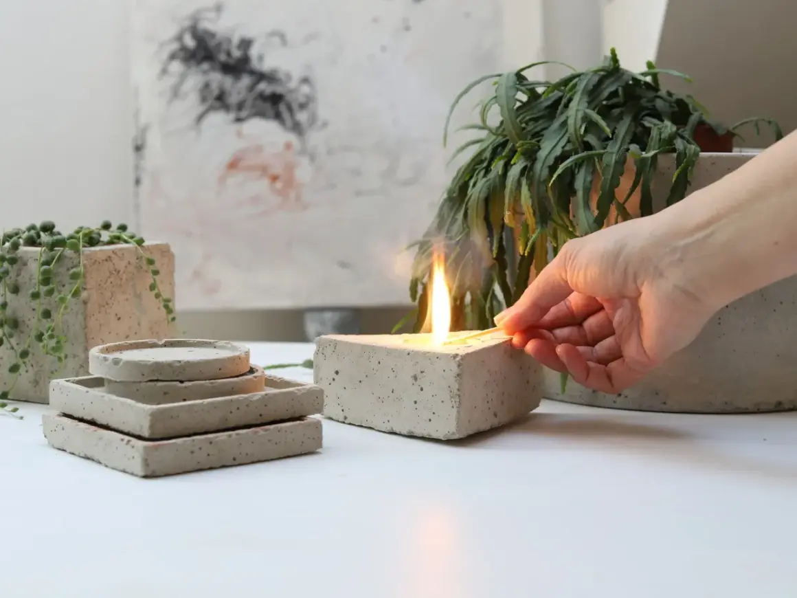 Accensione di una candela in un blocco di cemento, che ricorda come viene fatto il cemento. Piante e sottobicchieri in cemento completano la scena.