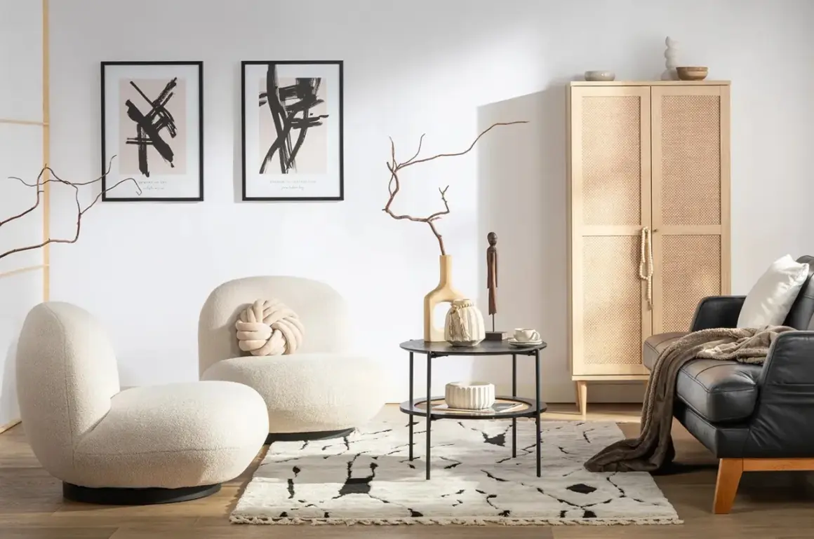 Przytulny salon w stylu hygge wnętrza. Jasne fotele, czarna skórzana kanapa, drewniana szafka z rattanowymi drzwiczkami i abstrakcyjne obrazy tworzą ciepłą atmosferę.