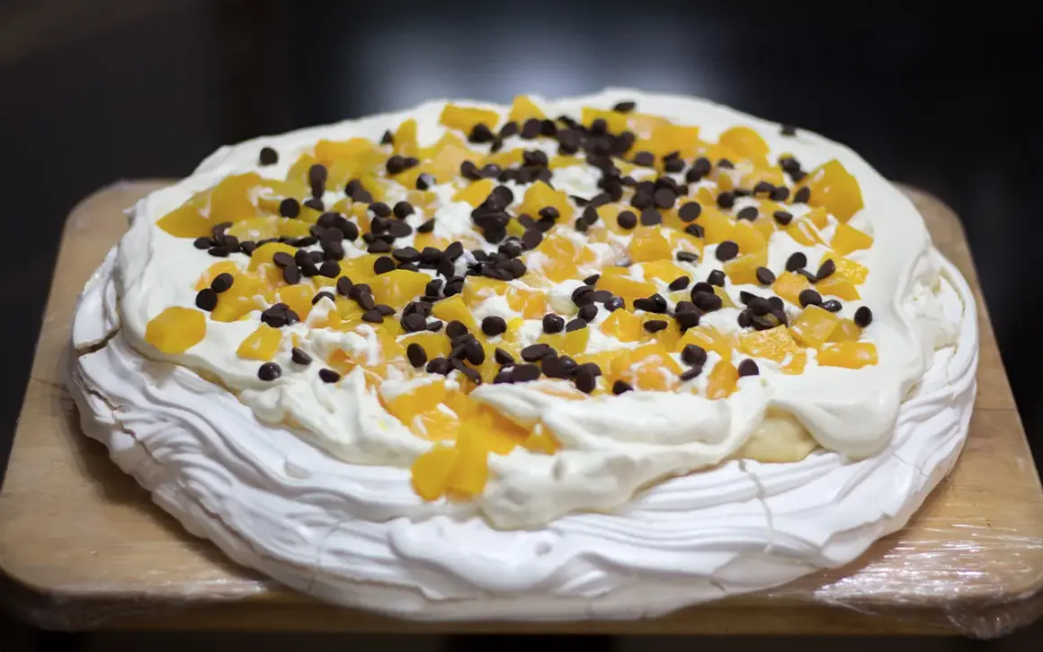 En härlig anna pavlova tårta med vispgrädde, persikobitar och chokladknappar.