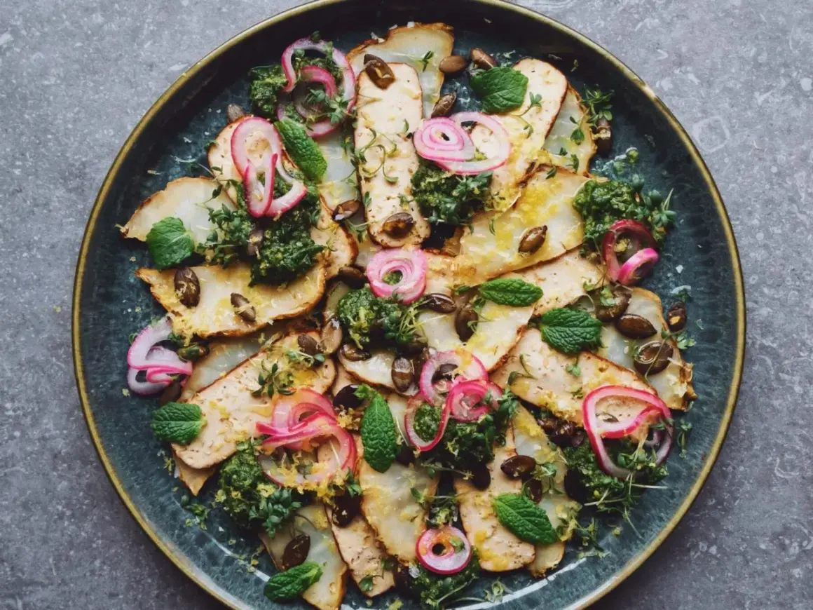 En vacker sallad med tunna skivor av rostad rotfrukt, toppad med grön örtolja, picklad rödlök, pumpakärnor och färska myntablad. Ett perfekt sallad recept för en lätt lunch.