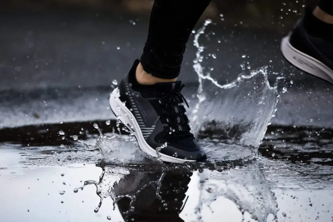 Un pied en basket noir et blanc éclabousse l'eau en courant sous la pluie.