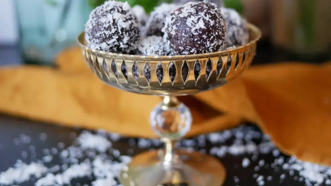 Nyttiga chokladbollar rullade i kokosflingor, serverade i en vacker guldfärgad skål. En perfekt, hälsosam godsak!