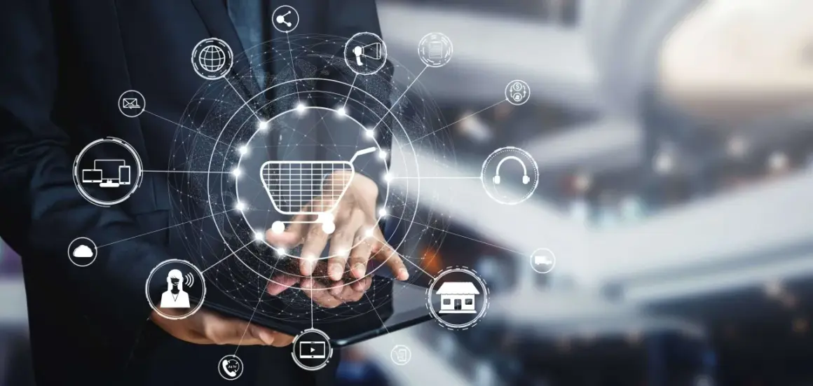 Biznesmen korzysta z tabletu, na którym wyświetla się grafika przedstawiająca koszyk zakupowy i ikony związane z e-commerce, takie jak drp ii.
