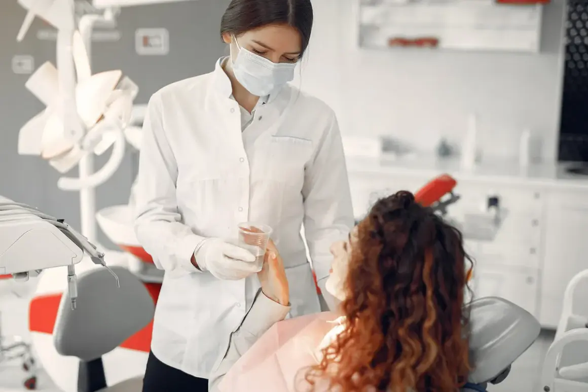 Dentystka w masce podaje wodę pacjentce. Bezpieczne leczenie kanałowe w ciąży jest możliwe.