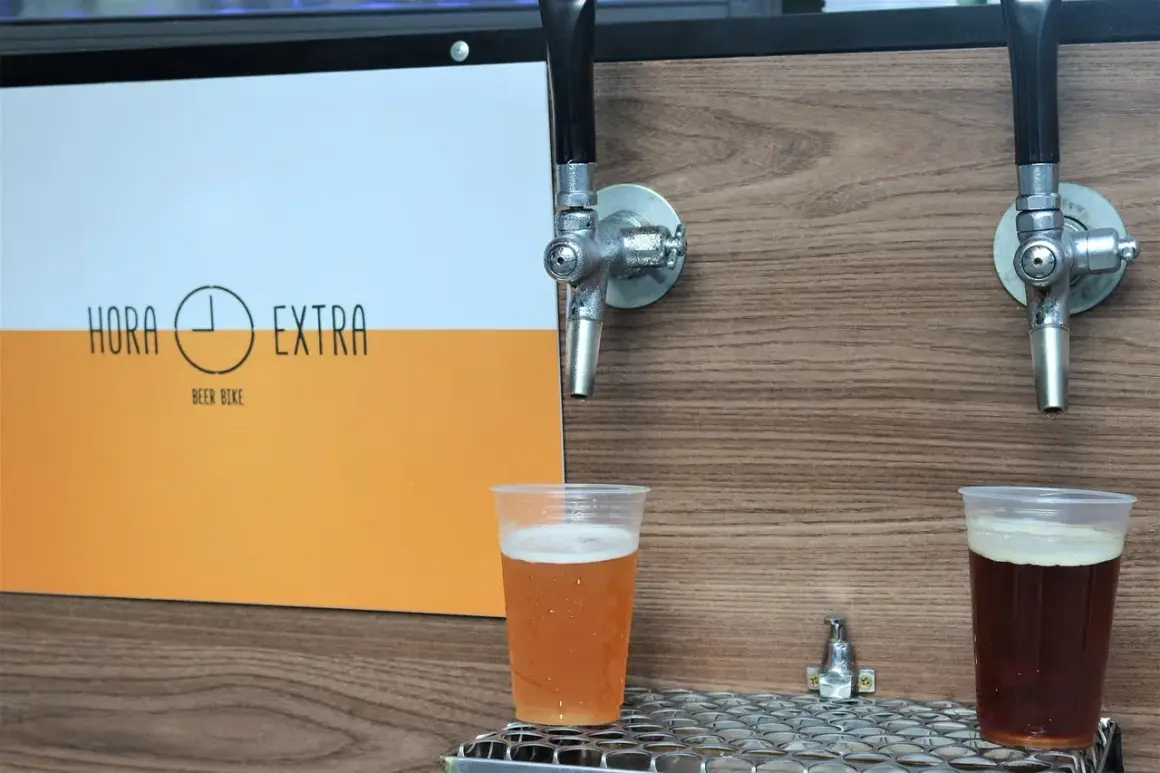 Dwa piwa w plastikowych kubkach pod kranikami. Jedno jasne, drugie ciemne. Logo "Hora Extra Beer Bike" z boku. Idealne na piwo bez chmielu.