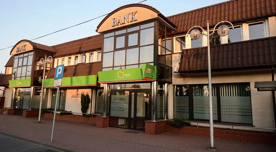Budynek banku z zielonym neonem i napisem "BANK". W tle widać parking, co może sugerować upadłe banki w Polsce.