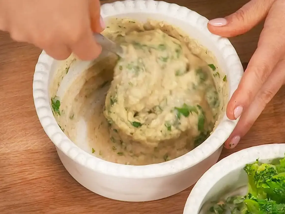En hand rör i en skål med krämiga refried beans och färska örter.