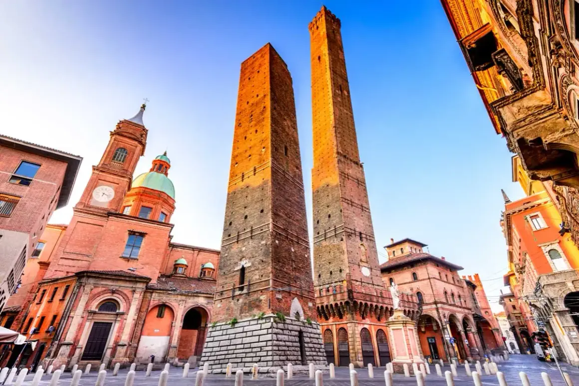 Le Due Torri svettano maestose nella piazza Maggiore di Bologna, con la Basilica di San Petronio sullo sfondo.