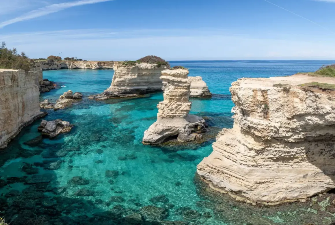 Klippformationer reser sig ur det turkosa vattnet vid Salento, Italien. En kajakpaddlare njuter av den vackra kusten.