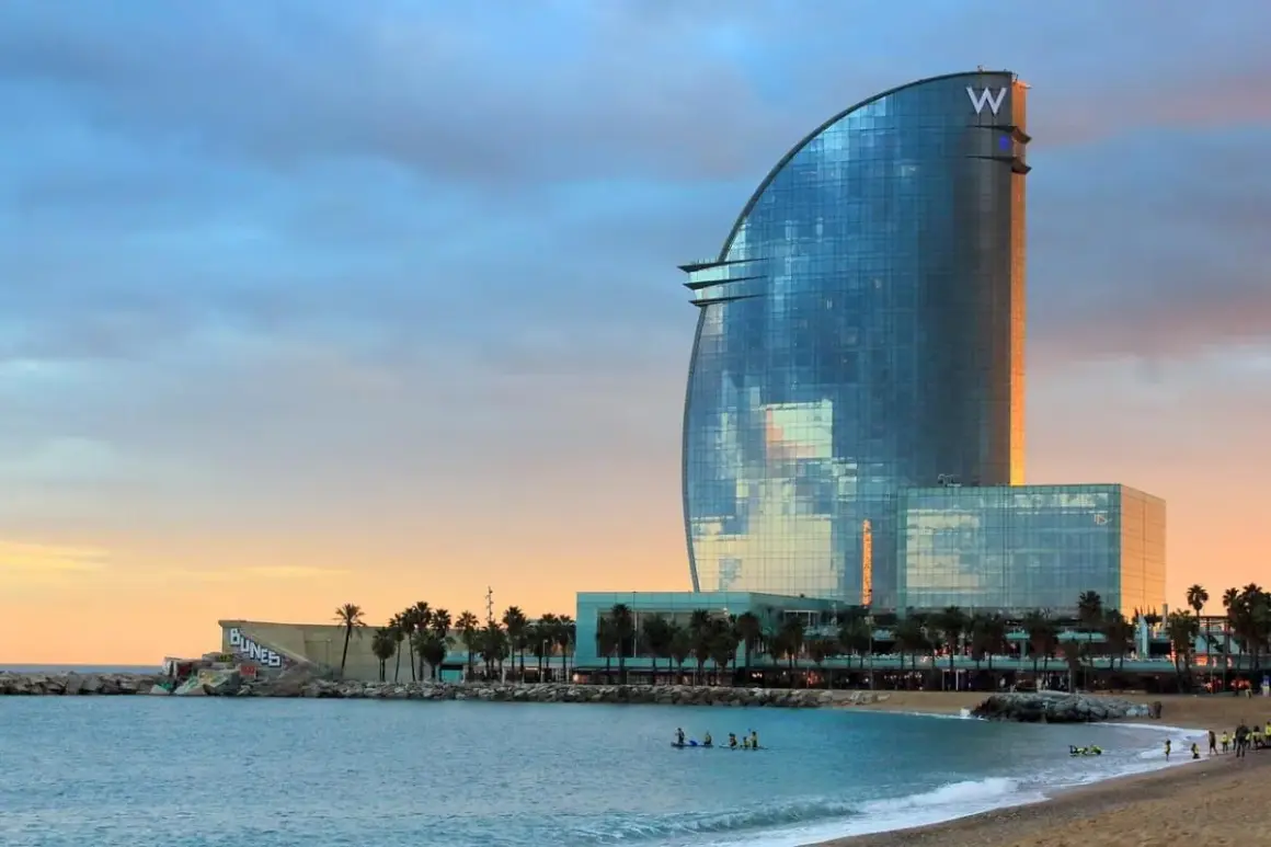 La spiaggia di notte a Barcellona, con il moderno Hotel W che riflette il cielo al tramonto.