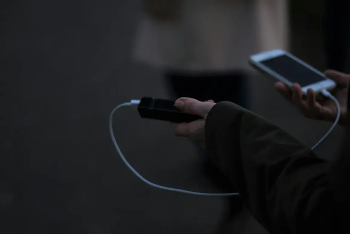 Ręka trzyma powerbank i smartfon, podłączone kablem. Elektronika w samolocie to klucz do rozrywki podczas podróży.