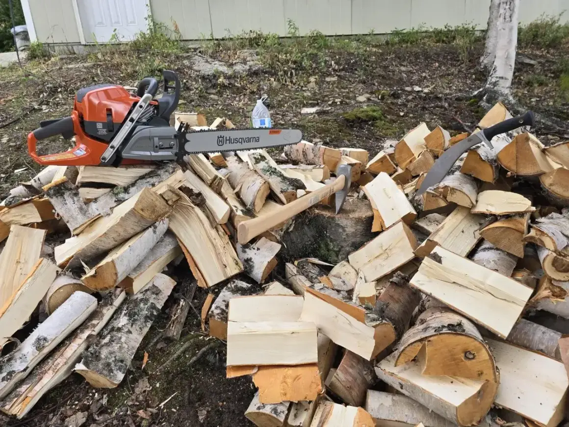 Piła łańcuchowa Husqvarna i siekiera leżą na stercie drewna. Do pracy przyda się olej Motul 800 2T do piły.