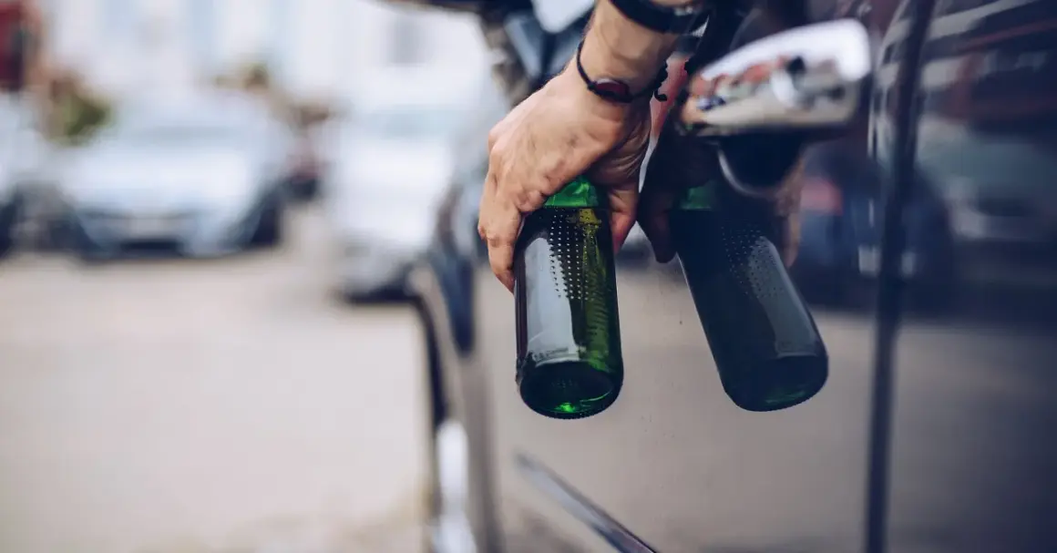 Hand hält Bierflaschen aus Autofenster. Die Frage "ab wie viel Promille ist man besoffen" wird hier thematisiert.