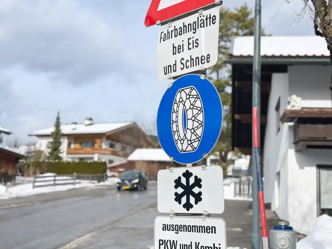 Verkehrsschilder weisen auf Fahrbahnvereisung bei Eis und Schnee hin. Ein blaues Schild zeigt eine Schneekette, ein weiteres ein Schneeflockensymbol.