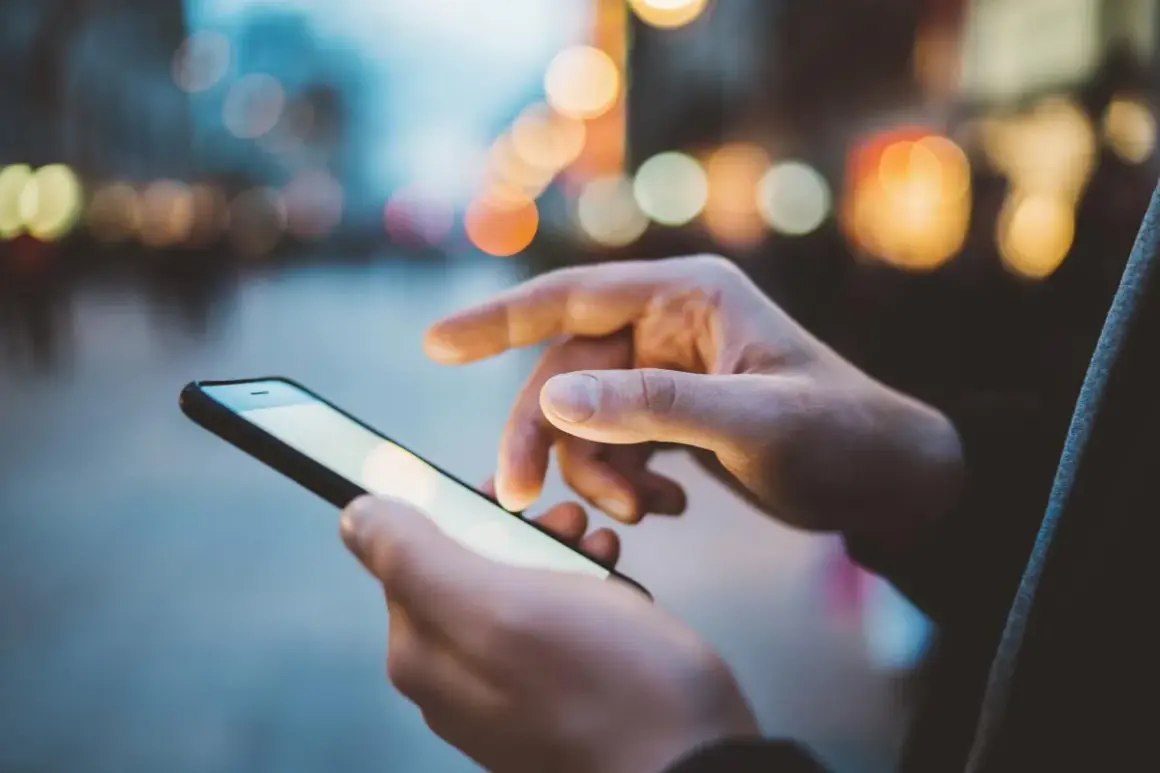 Dłonie trzymają smartfon, na ekranie którego widać rozmyte światła miasta. Szybki internet, jak APN Plus, pozwala na płynne przeglądanie.