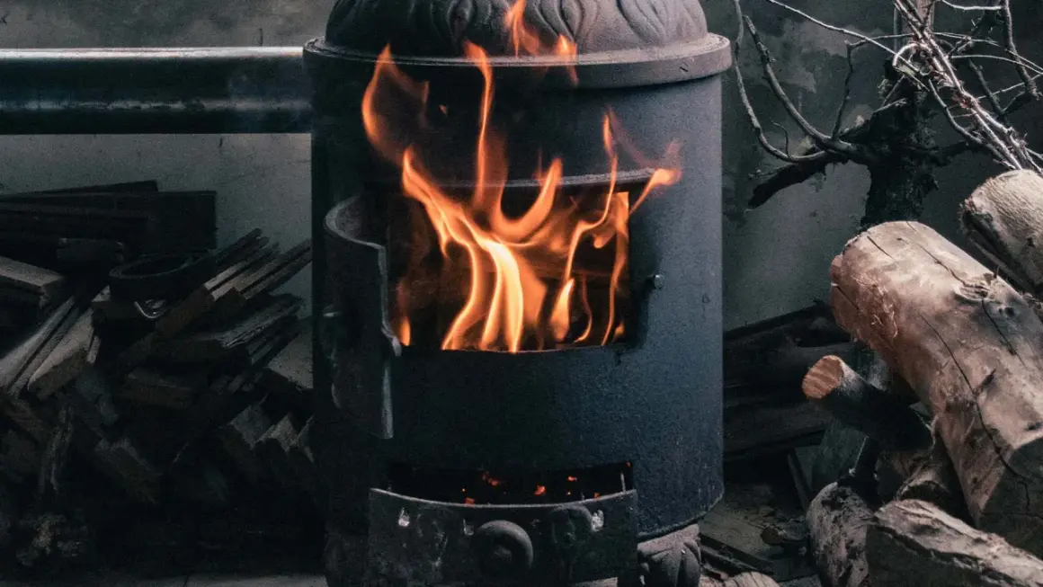 Ein Kaminofen brennt hell. Achte auf ausreichende Belüftung, um Sauerstoffmangel durch Kaminofen zu vermeiden. Holzscheite liegen daneben.