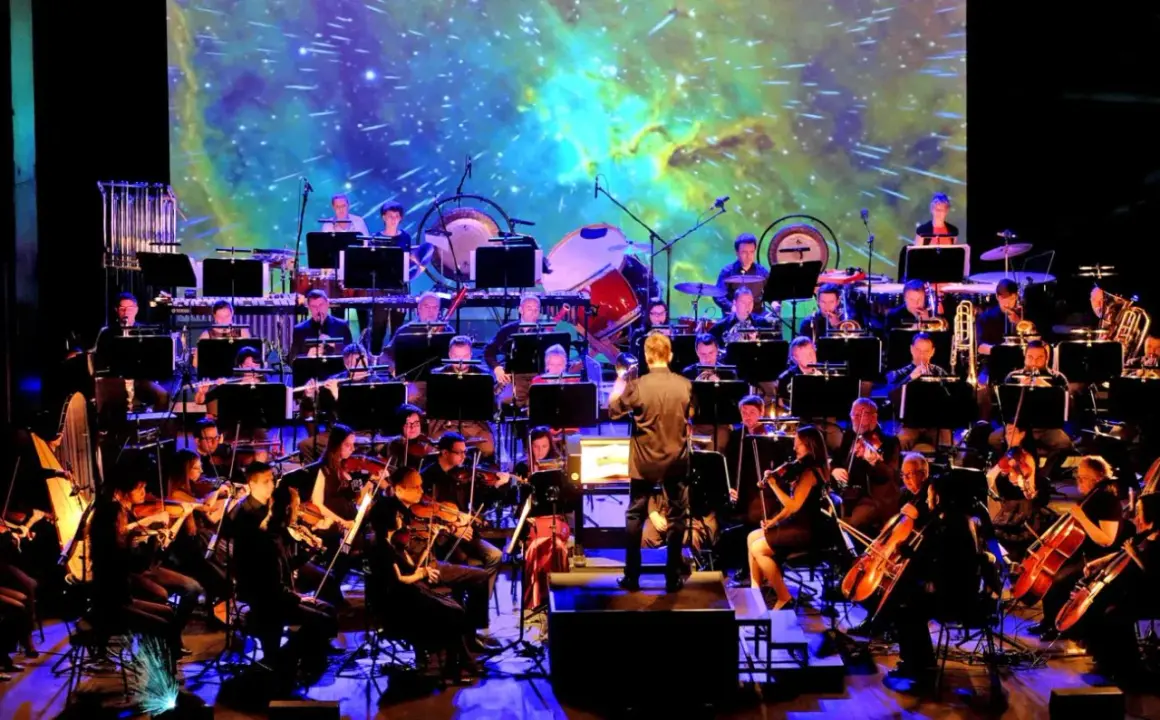 Orkiestra symfoniczna wykonuje najlepszą muzykę filmową wszech czasów na tle kosmicznej projekcji.