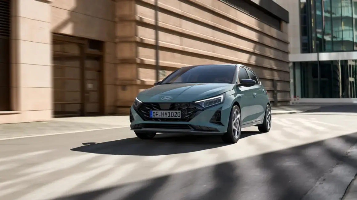 Nowoczesny Hyundai i20 w kolorze zielonym porusza się po miejskiej ulicy. To jeden z wielu stylowych modeli hyundaia.
