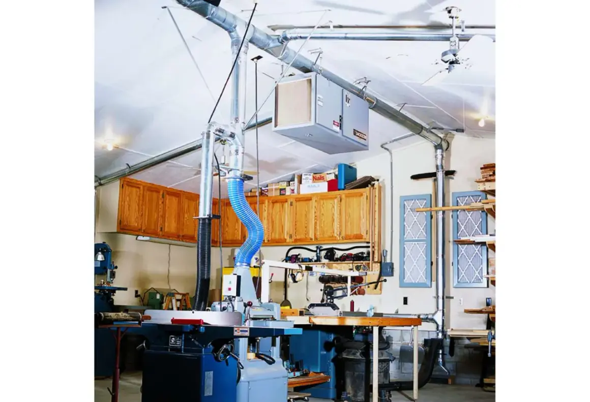 Atelier de menuiserie avec aspirateur à copeaux, tuyauterie et armoires en bois.