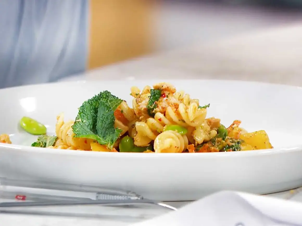 En läcker pastasallad med kyckling, gröna bönor och mynta på en vit tallrik.